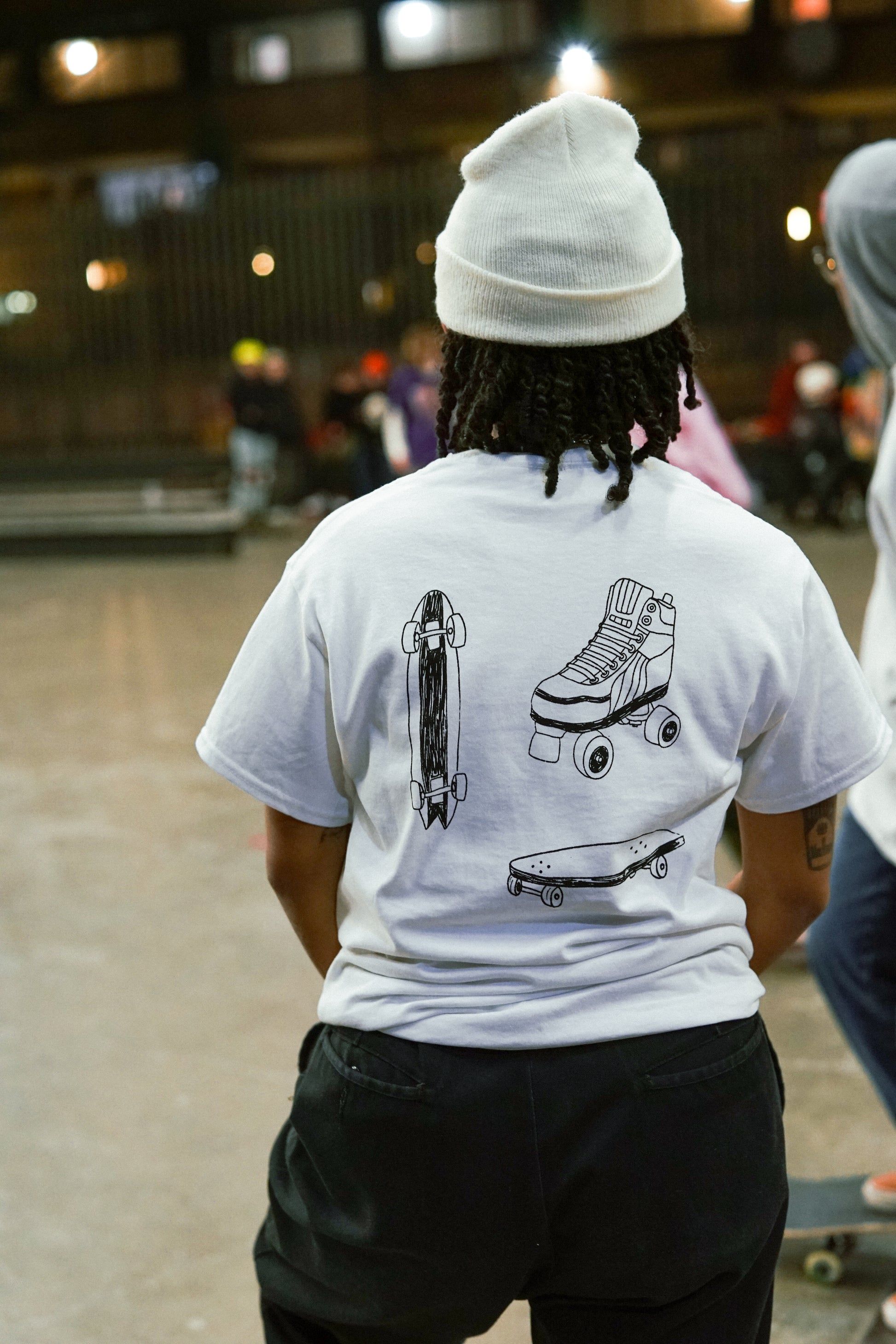 close up of a skater with their back to us, with the Transkaters t-shirt design in full view, of a skateboard, longboard and rollerskate 